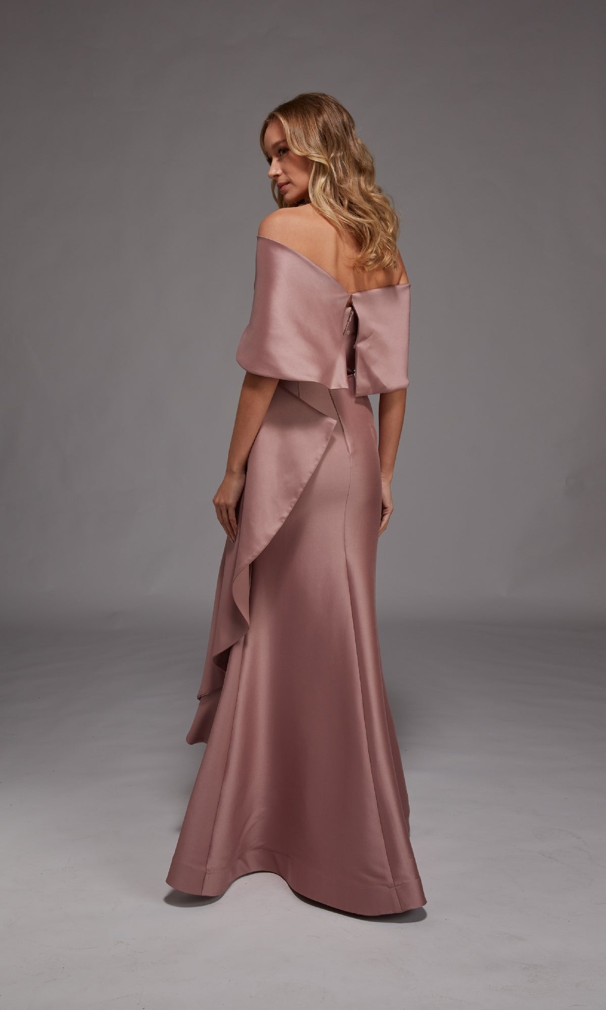 A woman poses against a plain backdrop, wearing the Alyce 27822 long formal dress—an off-the-shoulder mauve satin gown featuring a floor-length mermaid silhouette and a statement back bow detail.